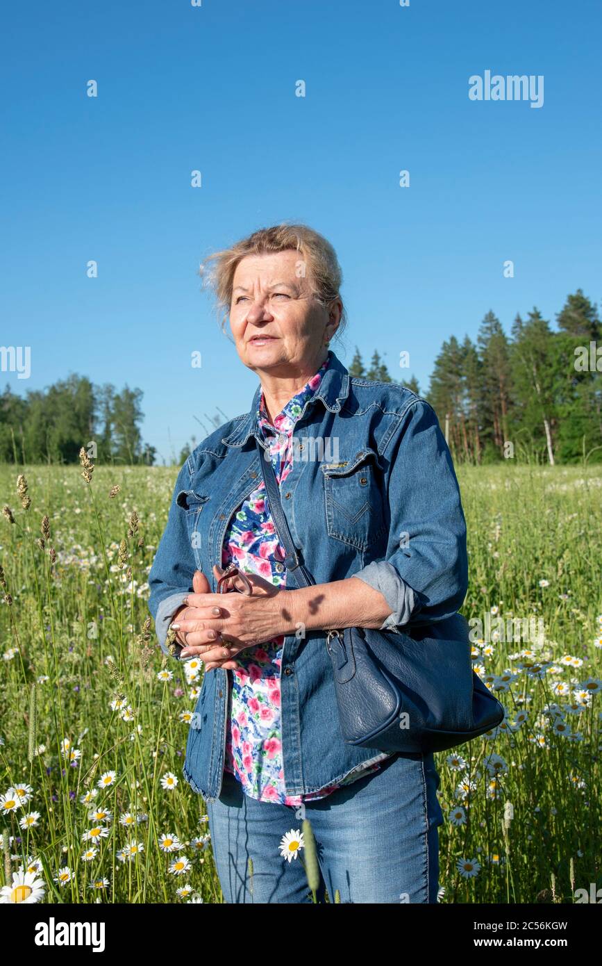 An elderly 65yearold woman in a denim suit stands in a chamomile