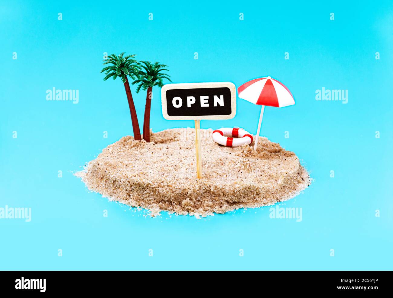 Miniature toy island with palm trees and a pole sign saying OPEN on a light blue background. Having summer break abroad during covid-19. Travel destin Stock Photo