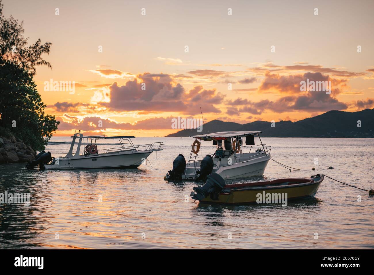 Fishing boats resting in sunset evening light near port of La Digue island, Seychelles. Praslin island on horizon. Stock Photo