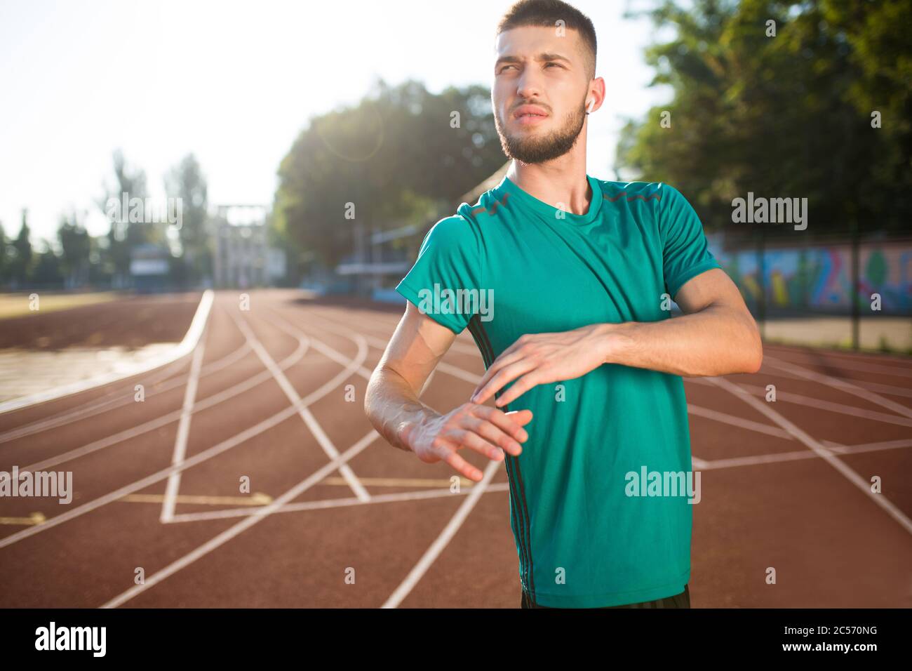 Young guy in wireless earphones thoughtfully looking aside spending time on treadmill of stadium isolated Stock Photo