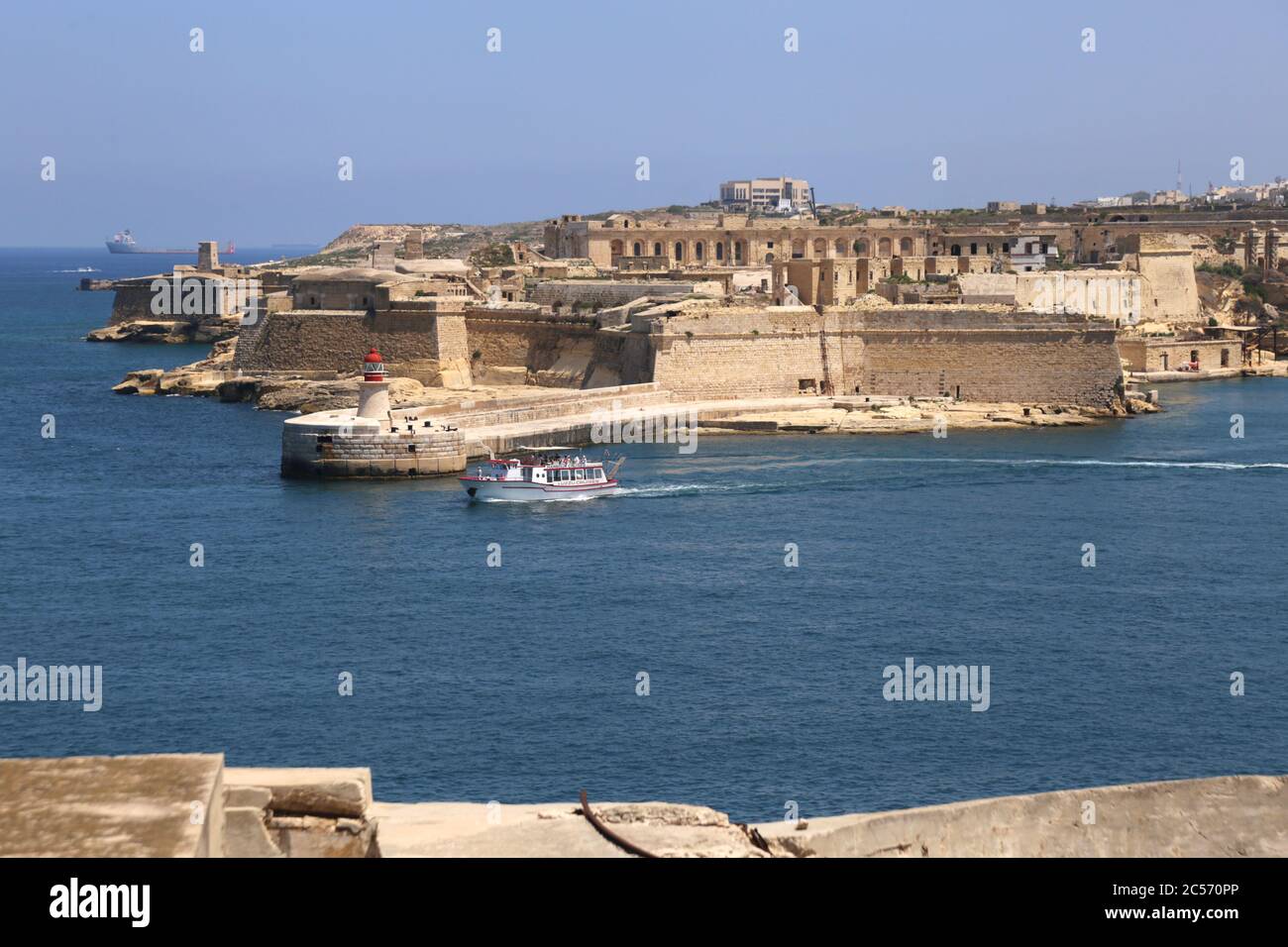 Valletta. Malta. Red old Lighthouse in Grand Harbour and breakwater bridge, Fort Ricasoli in Kalkara wiewed from Valletta. Stock Photo
