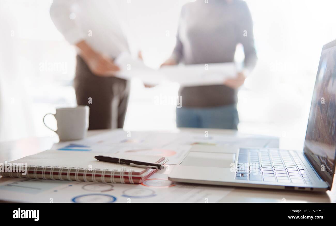 blur Close-shot of a pen and computer displaying financial data, business group standing in the background Stock Photo
