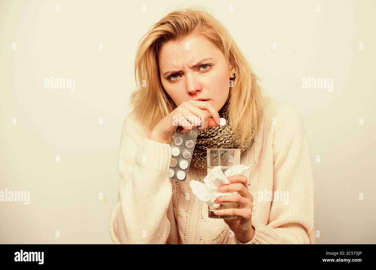 Pills to make her healthy. Ill woman treating symptoms caused by cold or flu. Medication and increased fluid intake. Unhealthy woman holding pills and water glass. Sick girl taking anti cold pill. Stock Photo