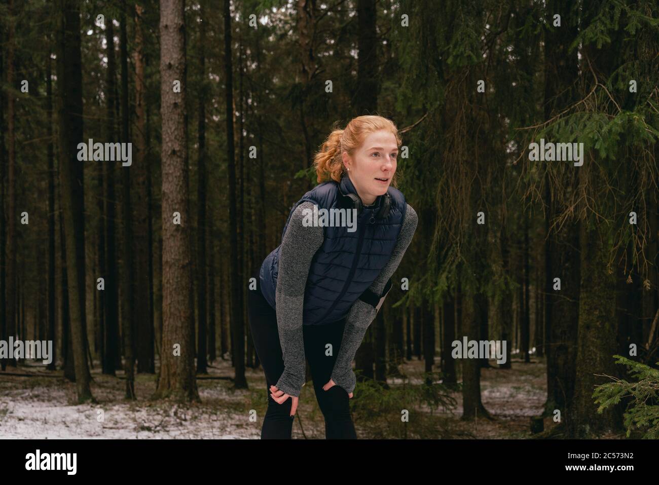 Female runner resting with hands on knees in snowy woods Stock Photo