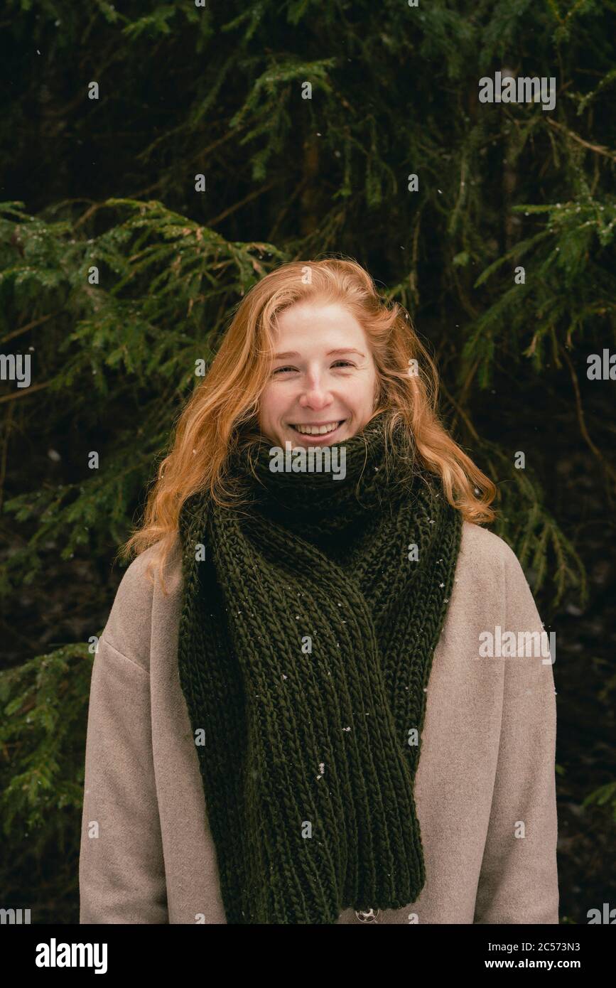 Snow falling over happy redhead woman in wool coat and scarf Stock Photo