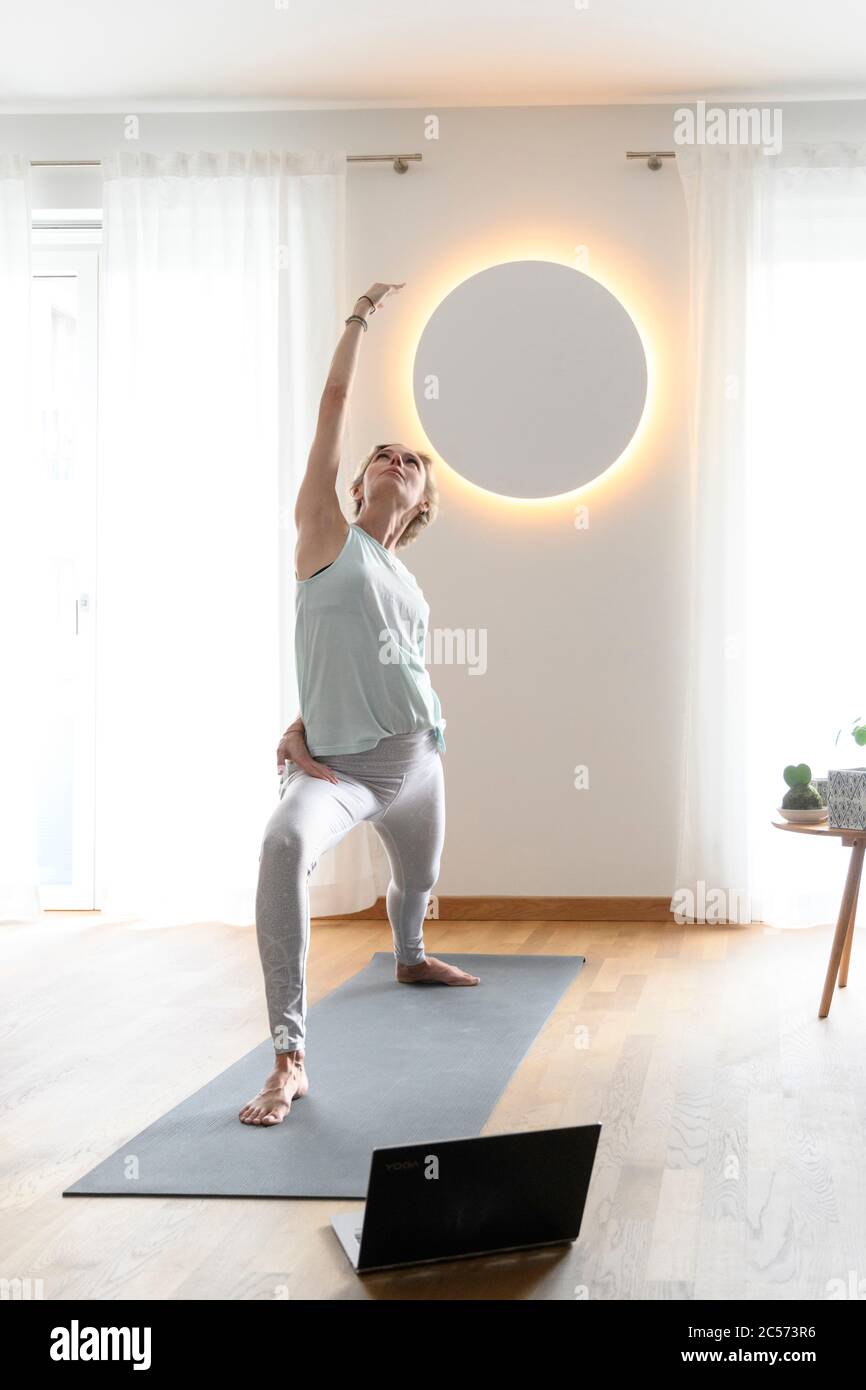 Woman 40+ practices yoga at home with notebook. Online yoga class. Stock Photo