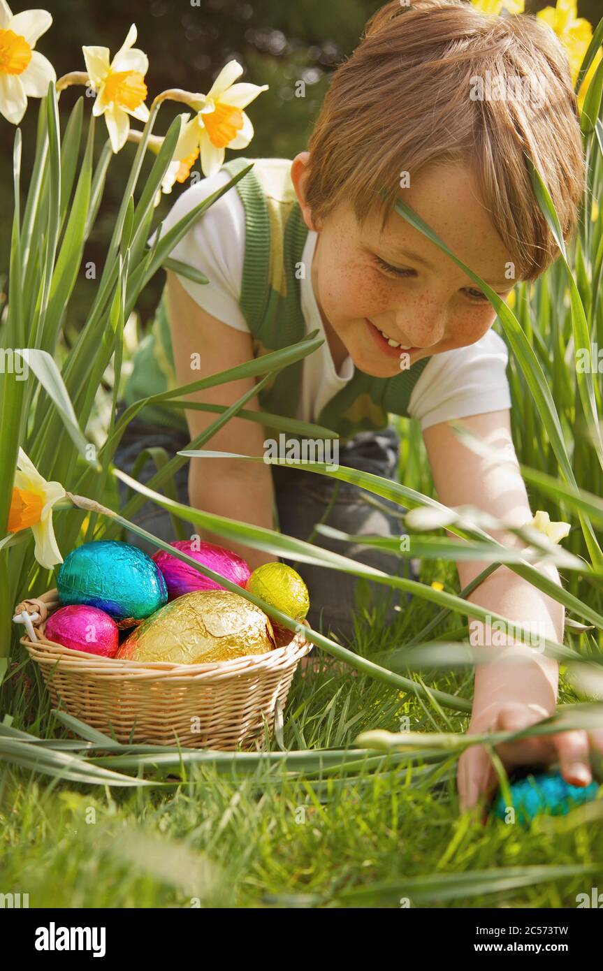 Smiling boy finding Easter egg candy among daffodils Stock Photo