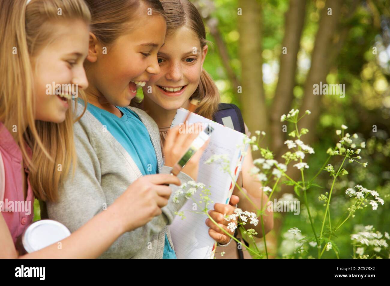 Smiling girls with magnifying glass examining flowers on field trip Stock Photo