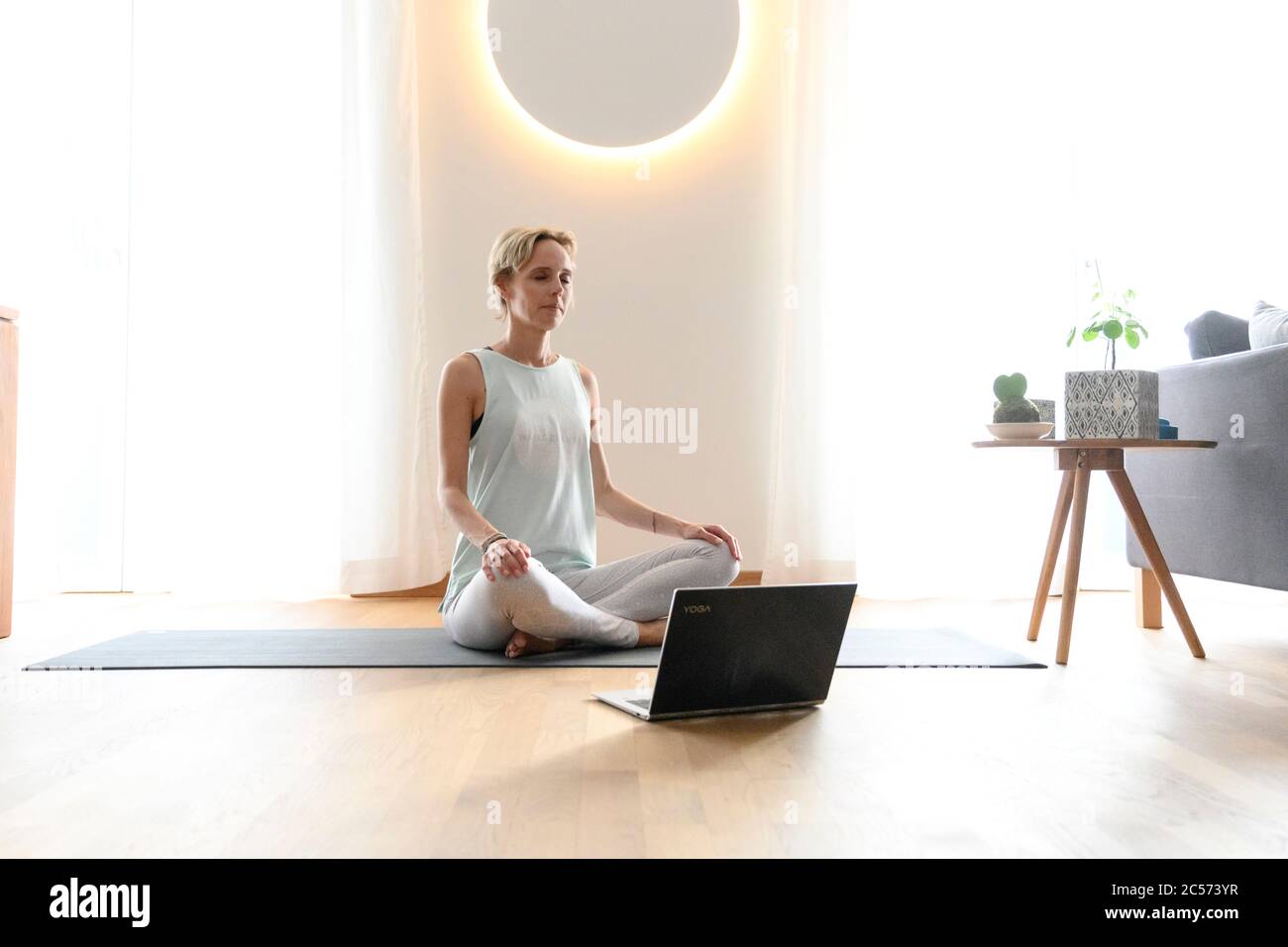 Woman 40+ practices yoga at home with notebook. Online yoga class. Stock Photo