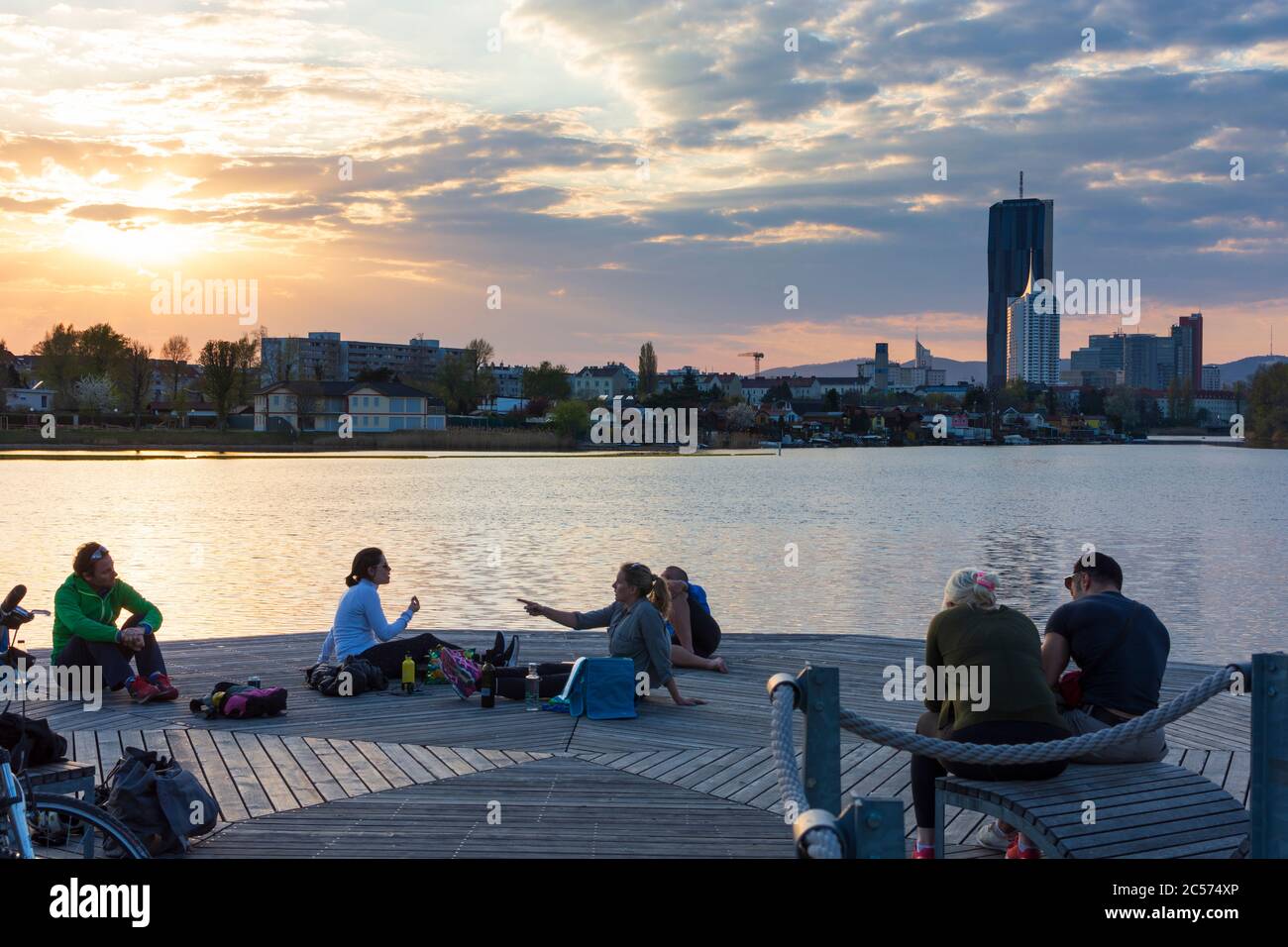 Vienna, people sitting at benches at wooden platforms at river Alte Donau (Old Danube) at sunset, in 22. Donaustadt, Wien, Austria Stock Photo