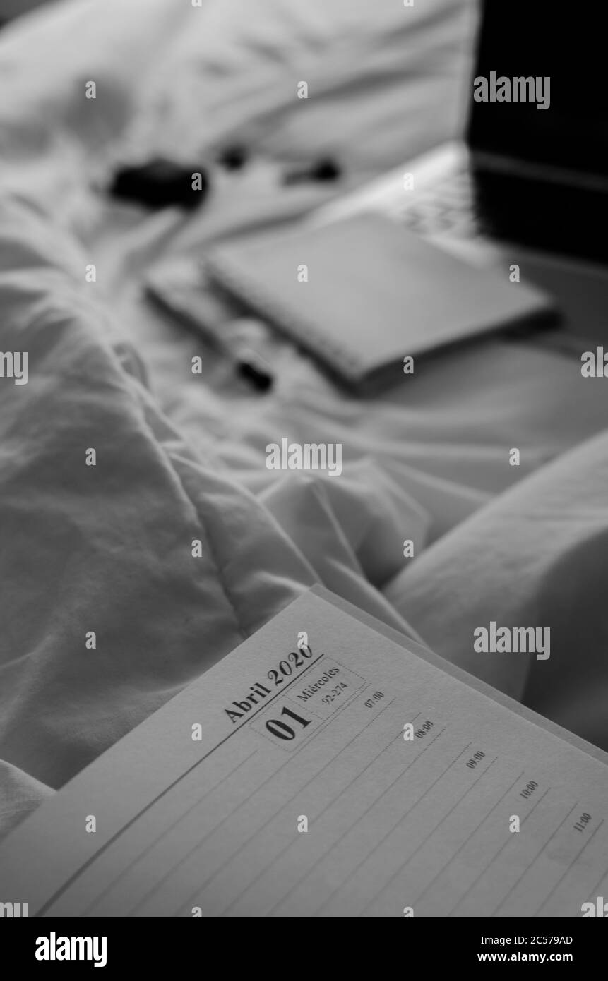 Grayscale shot of a 2020 calendar notebook along with a laptop, black wireless earbuds and pen Stock Photo