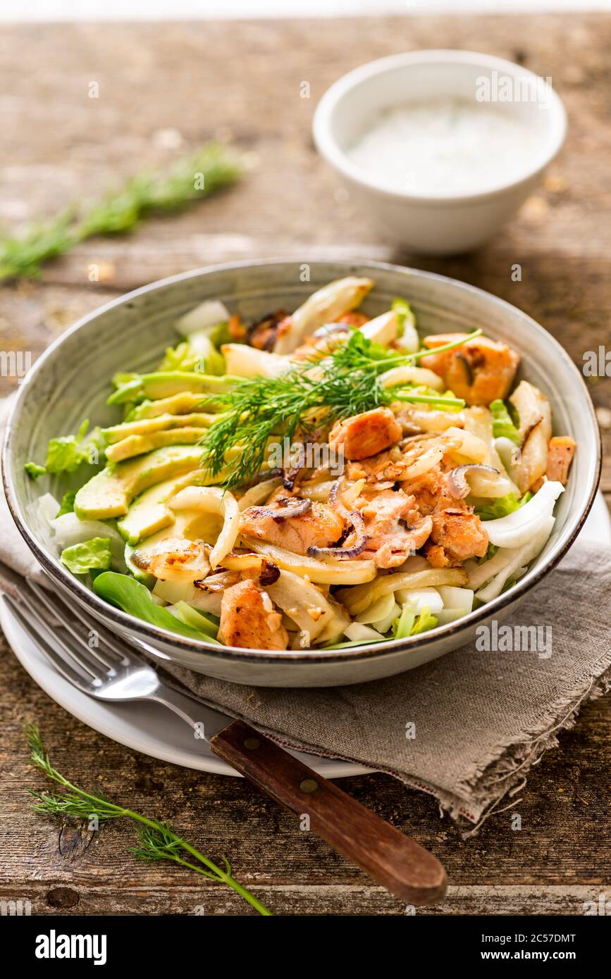 Main meal, salad bowl with salmon, oven-roasted fennel, fried onion, avocado, coconut yoghurt dressing Stock Photo