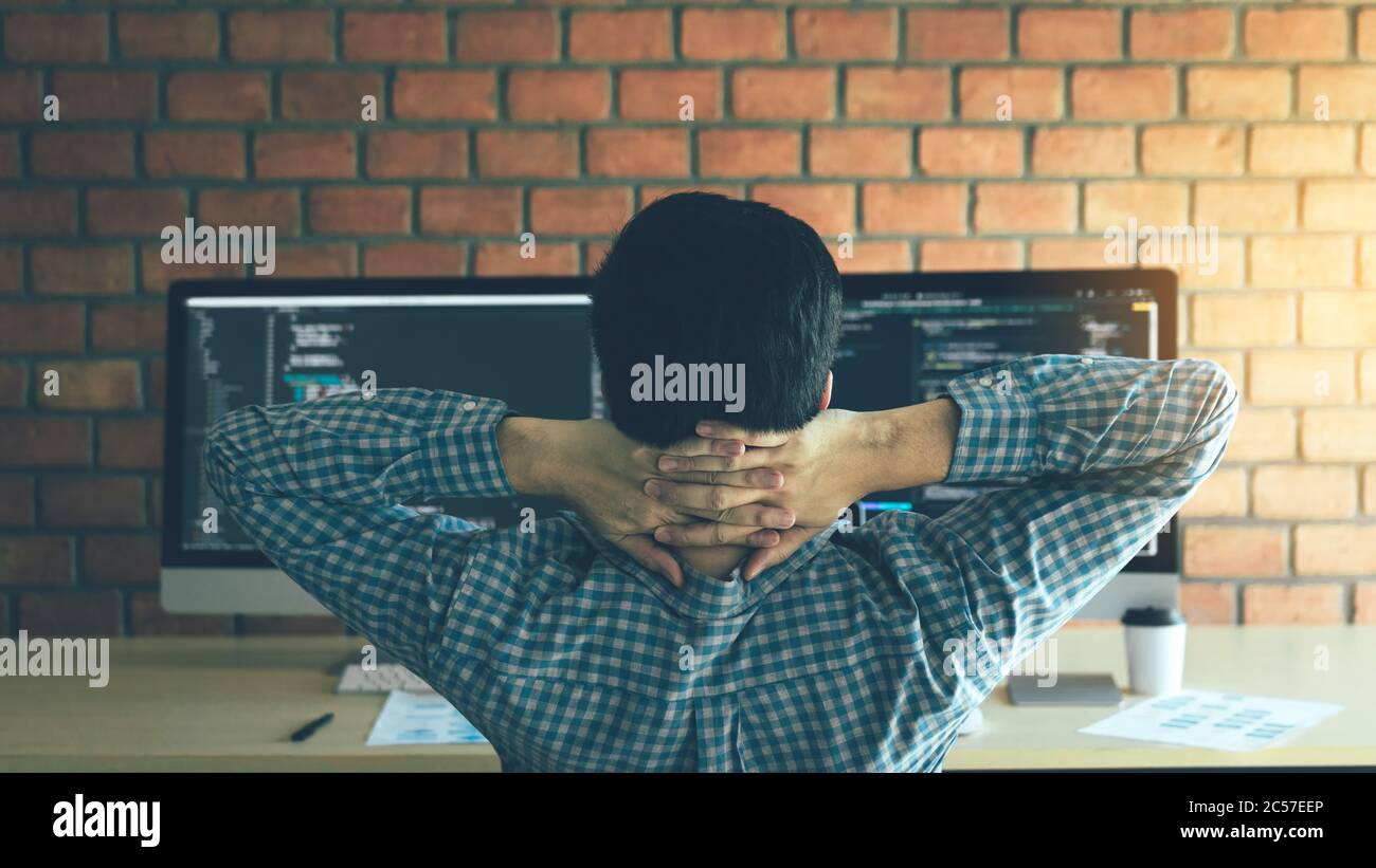 Asian programmers man are relaxing and looking at the code on the computer screen in the office. Stock Photo