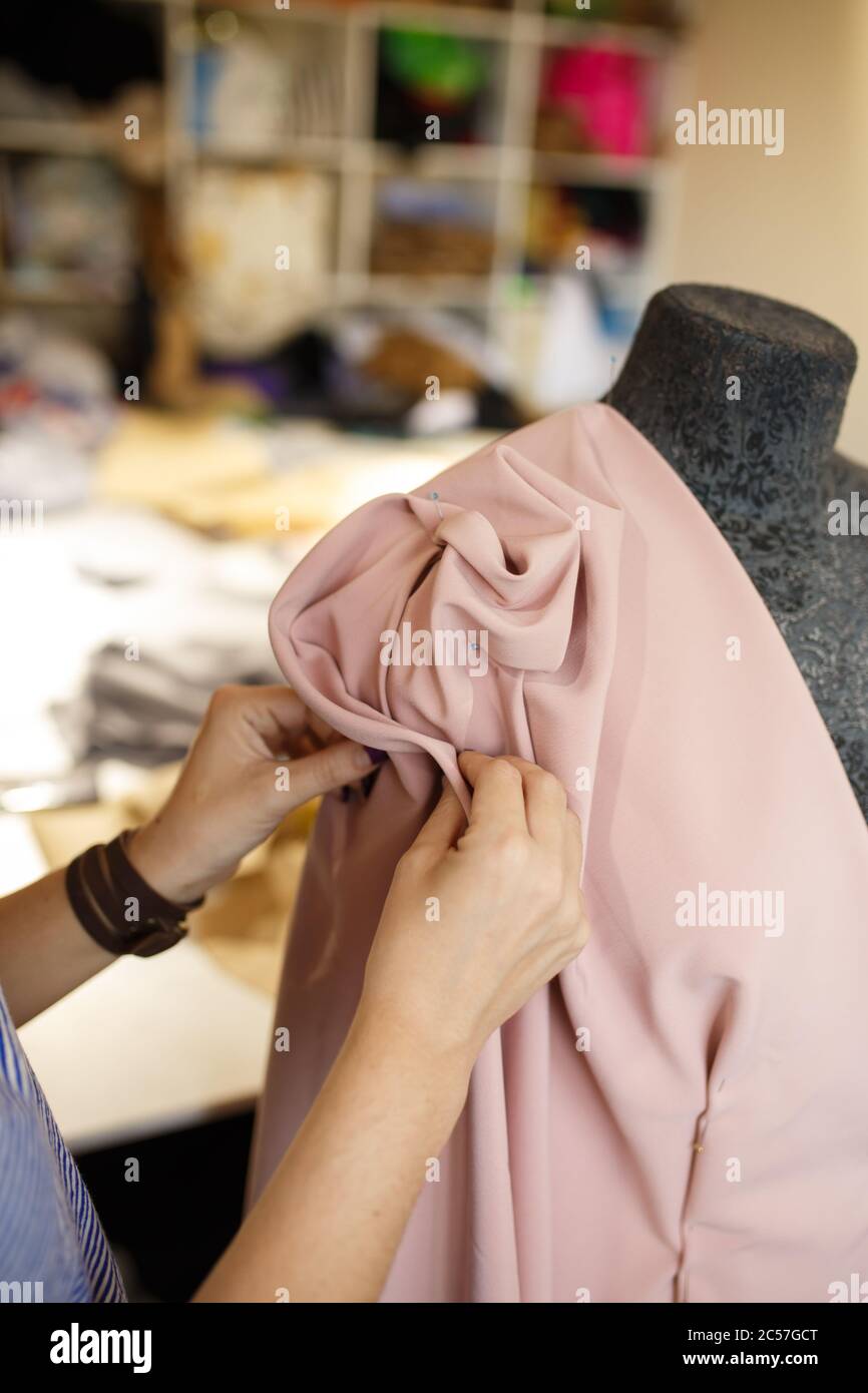 female dressmaker attach fabric to mannequin with needles. creating