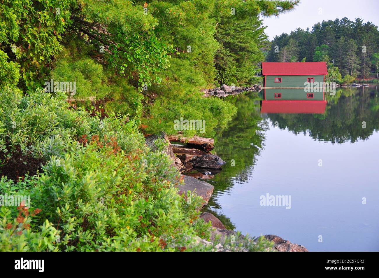 Red and green boathouse reflected in the still water of Lake Temagami, Ontario, Canada Stock Photo