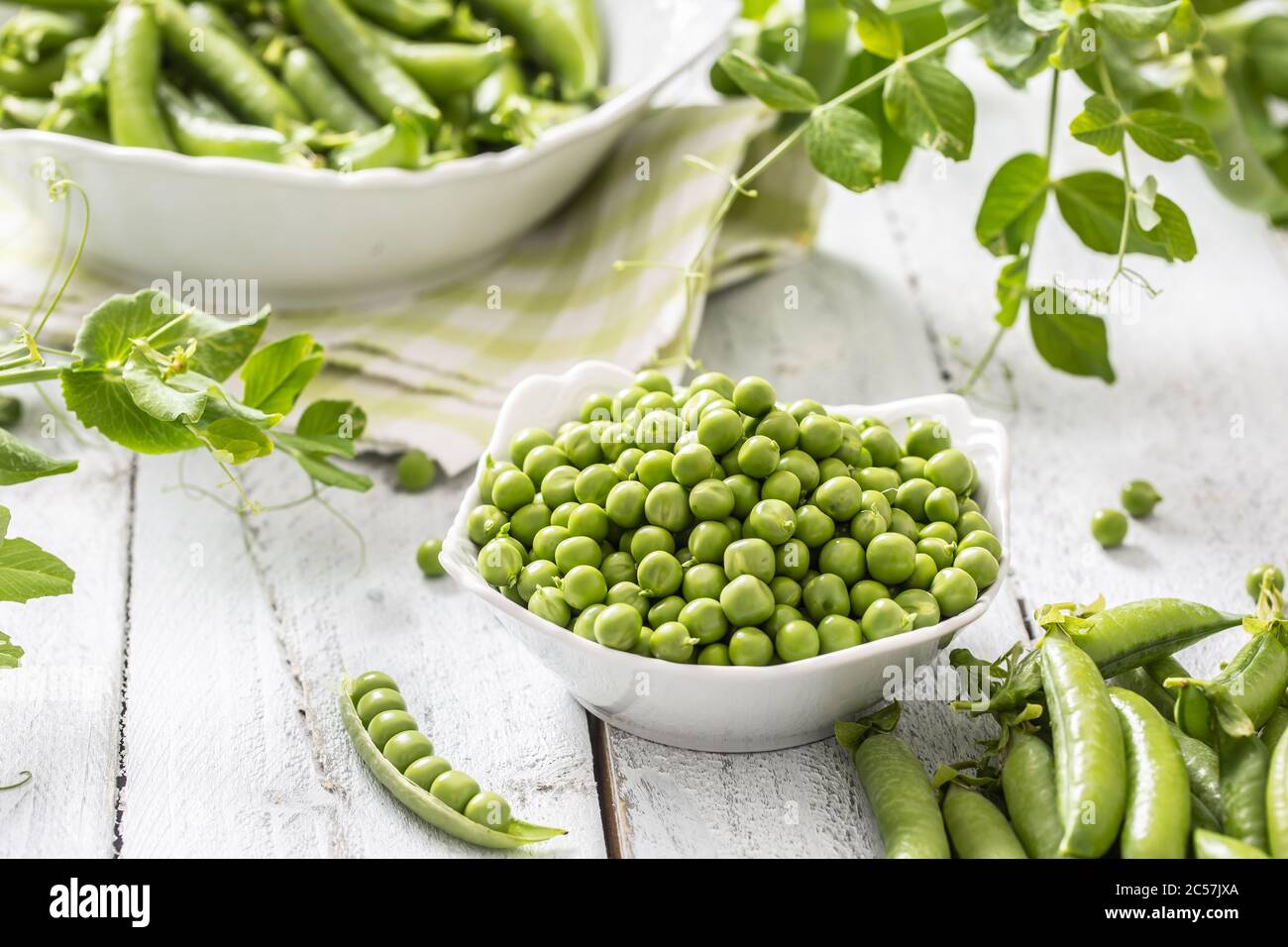 Green raw peas and pods in pocelain bow isolated on wooden table Stock Photo