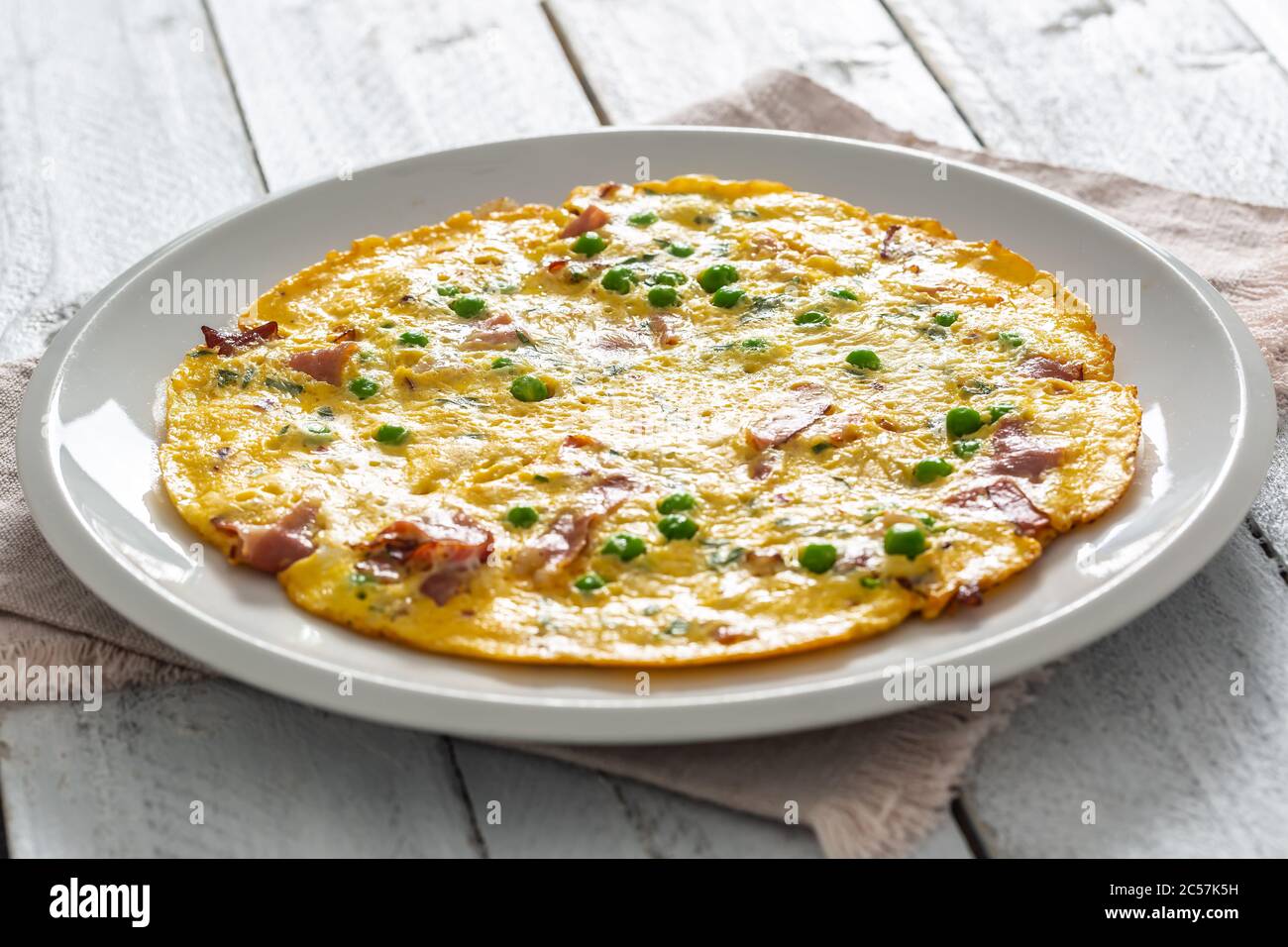 Omelette with prosciutto peas and herbs on white plate Stock Photo