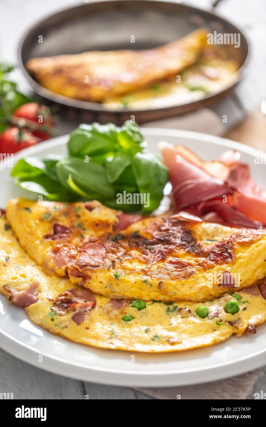 Omelette with prosciutto peas basil tomatoes and herbs on white plate Stock Photo
