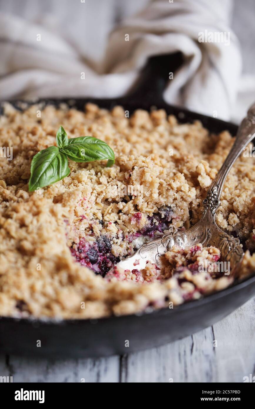 Sweet homemade Blackberry and Blueberry Basil Cobbler baked in a cast iron pan and topped with a golden oatmeal crisp over a rustic white wood table. Stock Photo