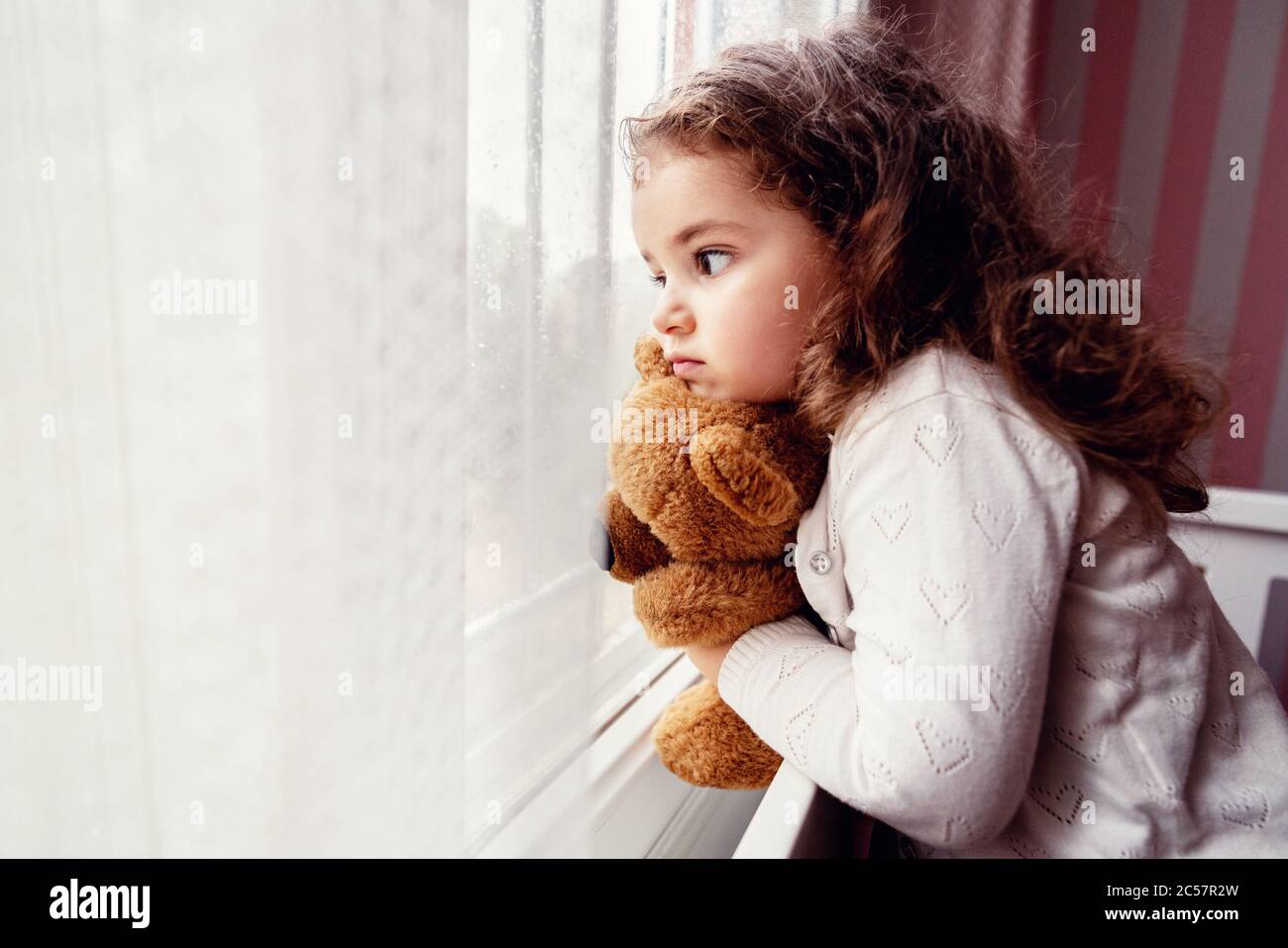 Little cute girl is watching from window to the rain with sadness get bored. . High quality photo Stock Photo