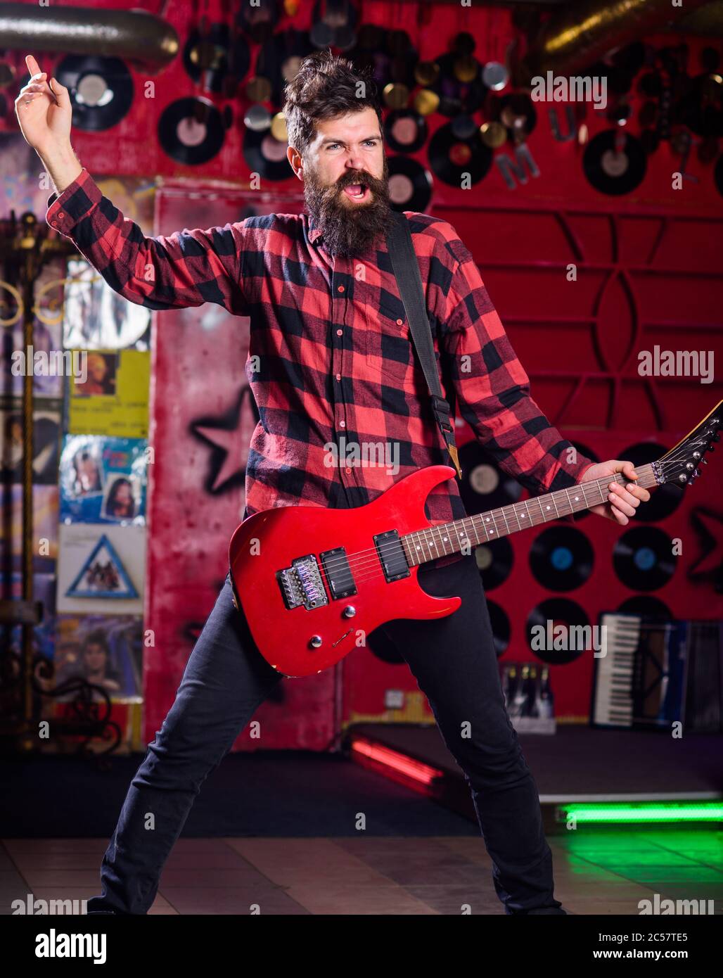 Frontman concept. Musician full of energy, soloist, singer. Musician with beard play electric guitar. Man with shouting face play guitar, singing song, play music, music club background. Stock Photo