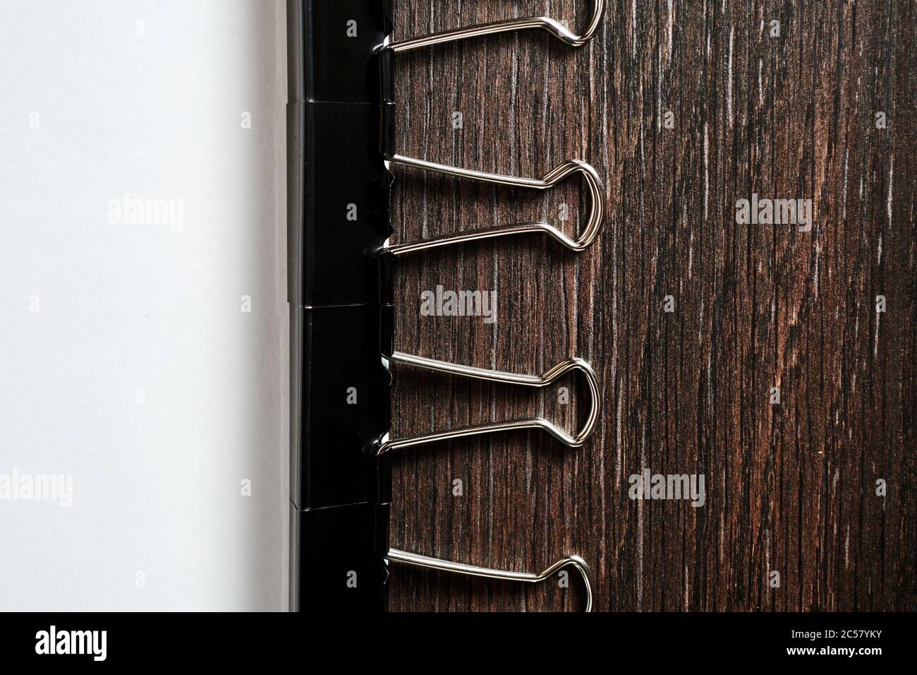 The chain of black metallic paper clips pins the white paper sheet on the wooden table in the home office Stock Photo