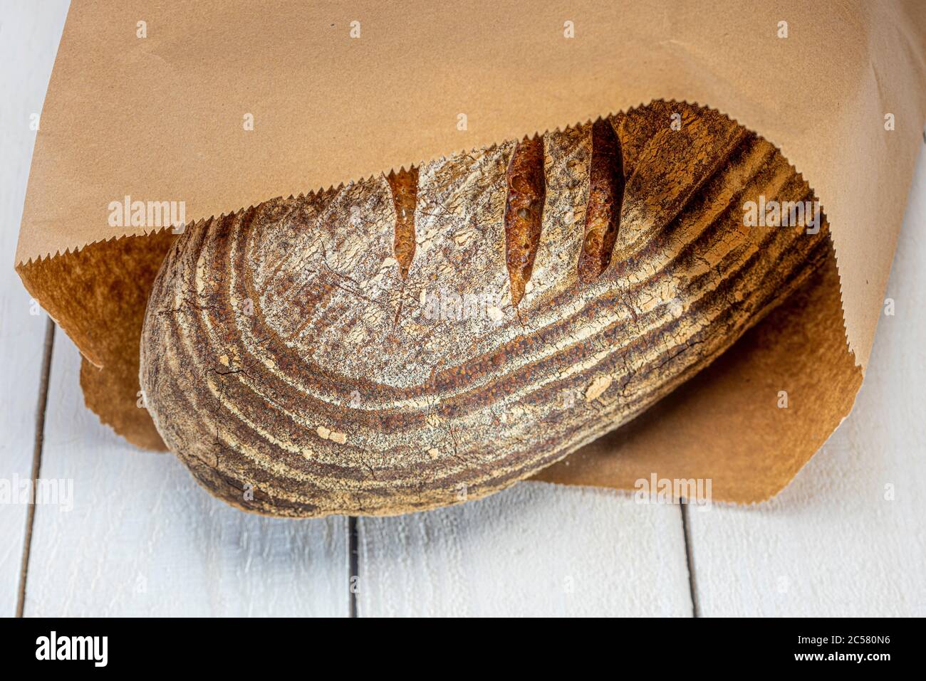 Freshly baked sourdough loaf of bread in brown paper bag on whitewashed ...