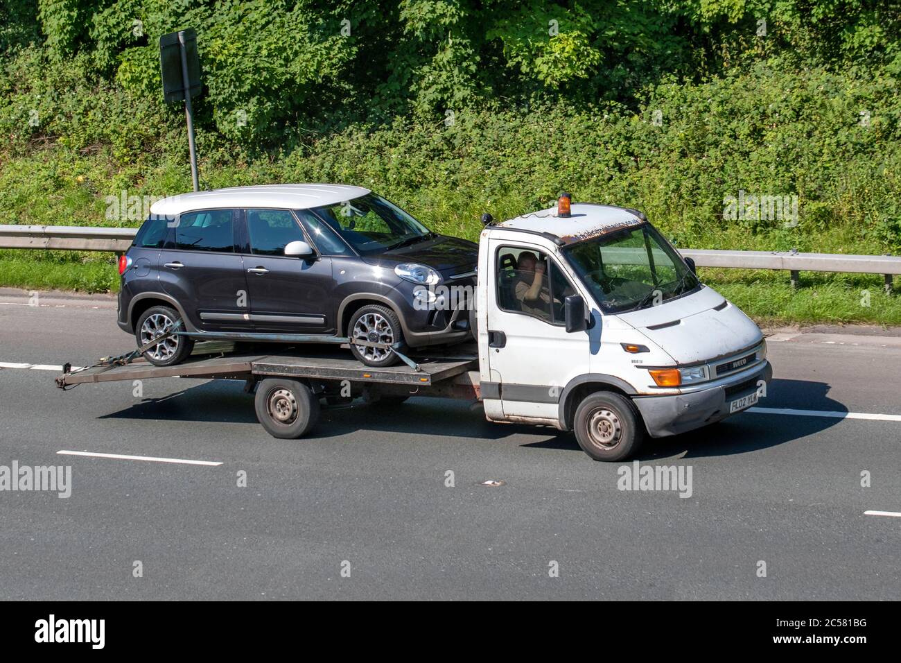 Old 2002 Iveco flat bed car carrier; Vehicular traffic moving vehicles, cars driving vehicle on UK roads, carrying Fiat 500 plus motors, motoring on the M6 motorway highway network. Stock Photo