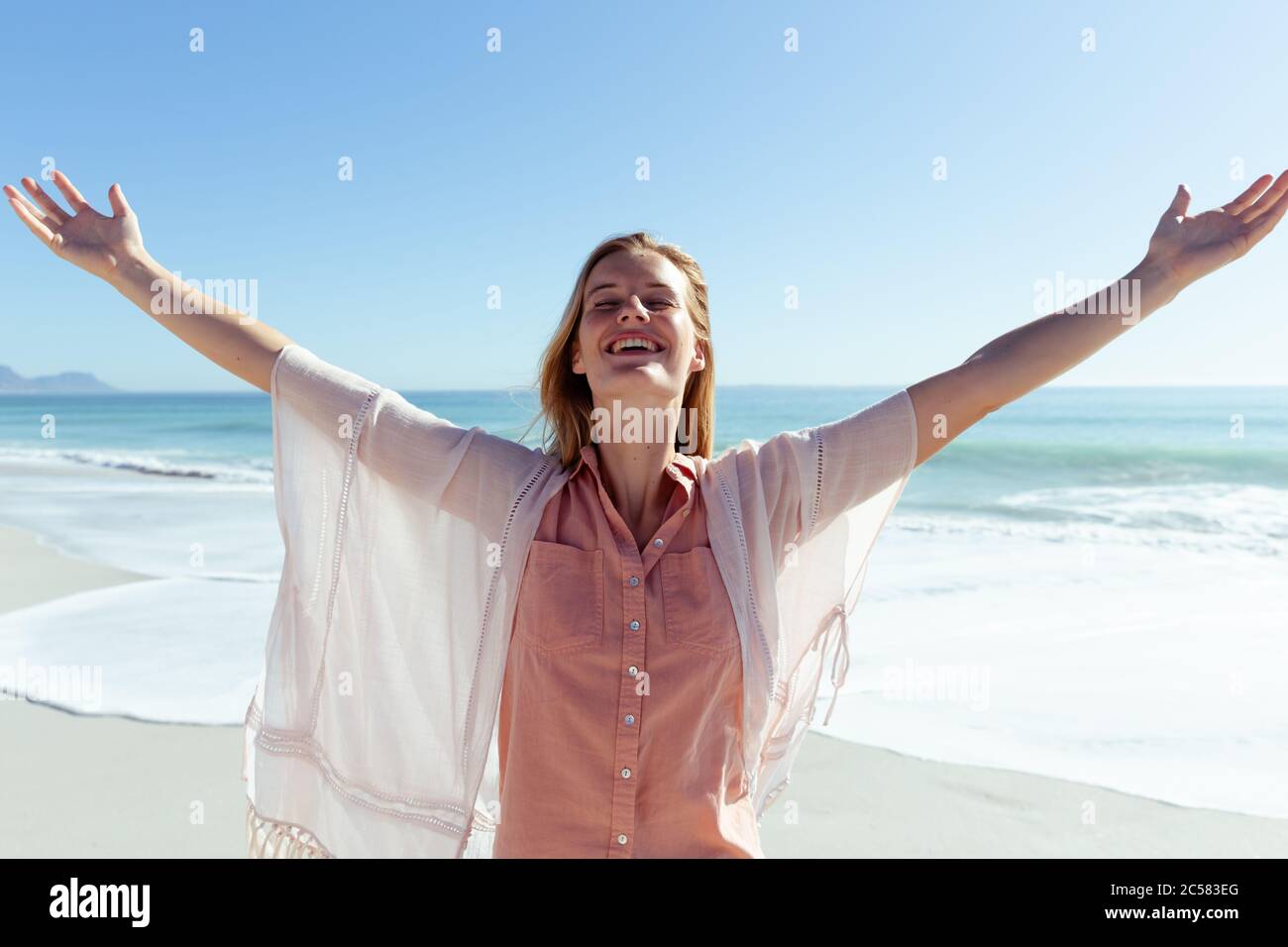 Happy woman standing with her arms wide open at the beach Stock Photo