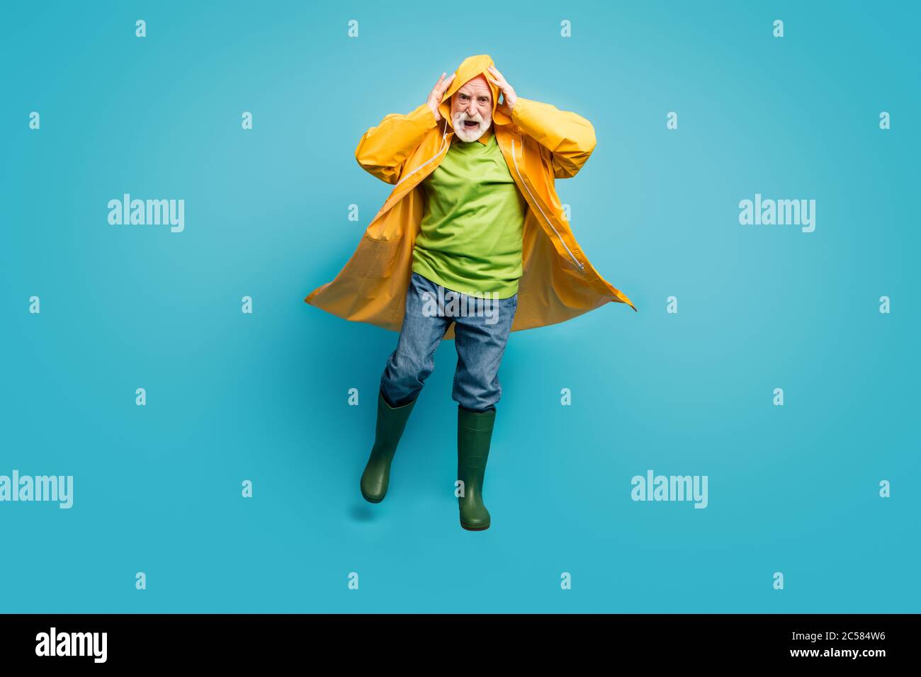 Full length photo of rushing home grandpa walk run street puddles rainy weather slippery wet road wear jeans jumper gum boots yellow raincoat isolated Stock Photo