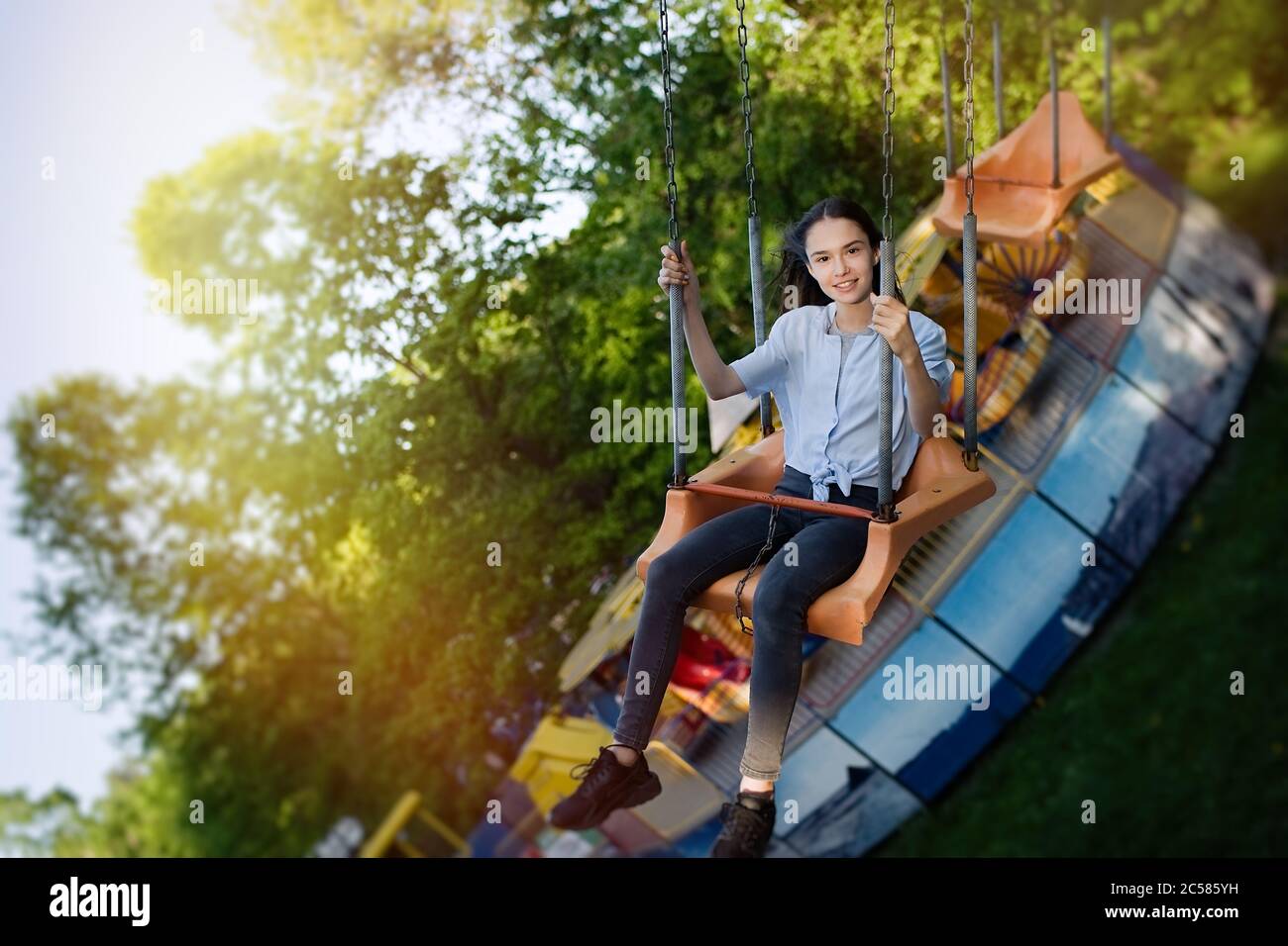 Happy child teenage girl riding chain carousel swing at amusement park Stock Photo