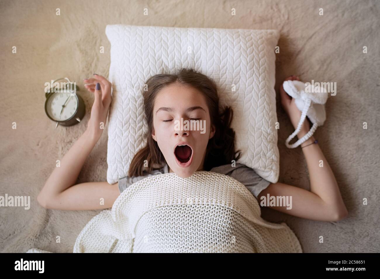 Sleepy teenager girl turning alarm off in the morning while lying in