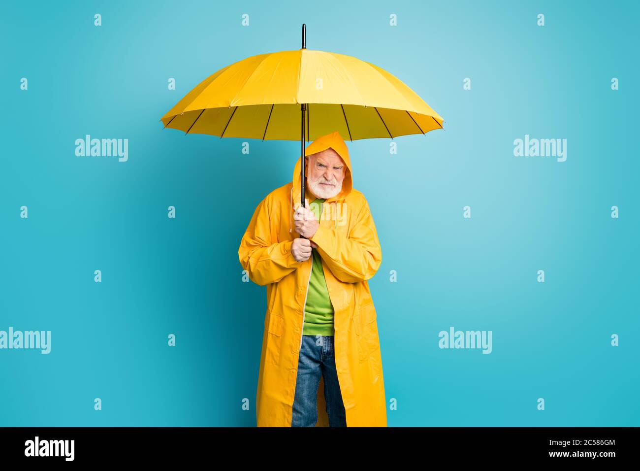 Portrait of his he dissatisfied irritated annoyed grey-haired man mushroomer wearing yellow overcoat dislike bad weather cyclone isolated over bright Stock Photo