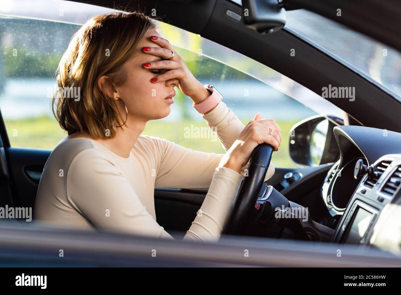Exhausted woman driver feeling headache, sitting inside her car, keeping hand to head and feeling anxiety. Stop after driving car in traffic jam.Blood Stock Photo