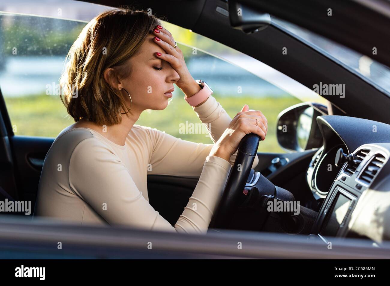Exhausted woman driver feeling headache, sitting inside her car, keeping hand to head and feeling anxiety. Stop after driving car in traffic jam.Blood Stock Photo