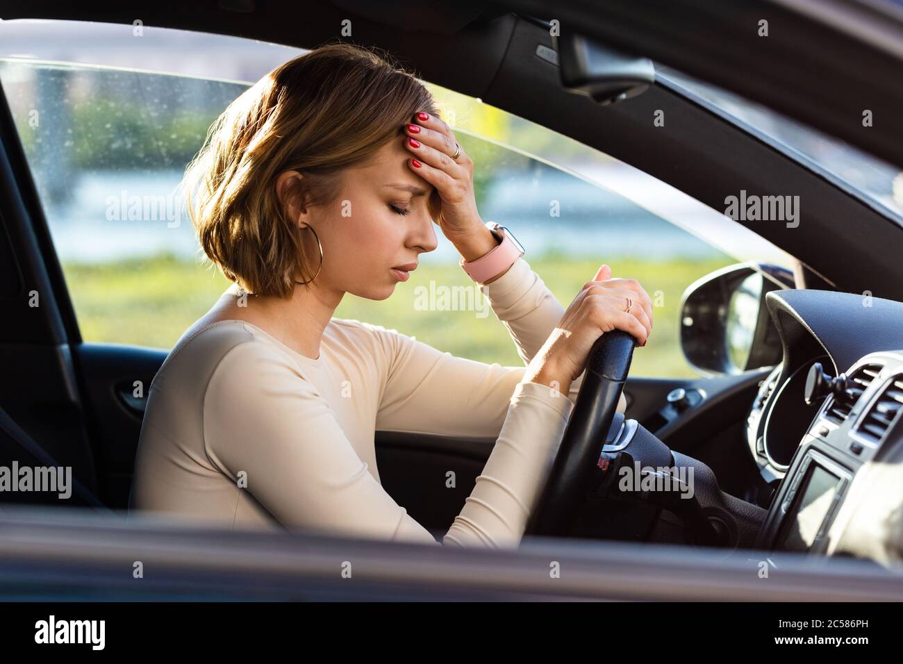 Exhausted woman driver feeling headache, sitting inside her car, keeping hand to head and feeling anxiety. Stop after driving car in traffic jam.Blood Stock Photo