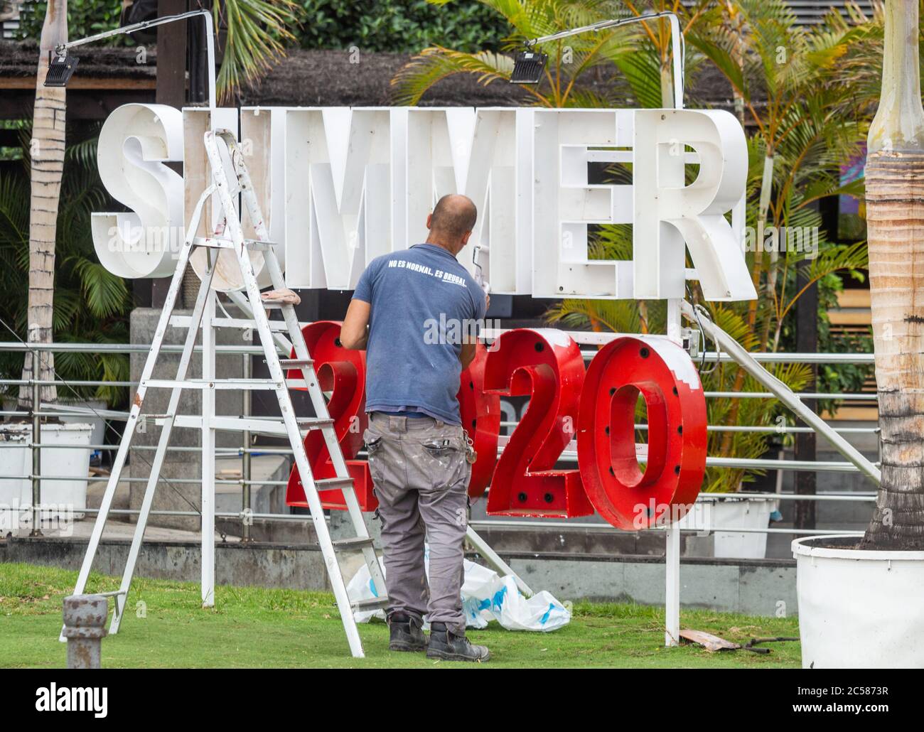 Las Palmas, Gran Canaria, Canary Islands, Spain. 1st July, 2020. A man  paints a summer 2020 sign outside a beach bar overlooking a tourist free  city beach in Las Palmas on Gran