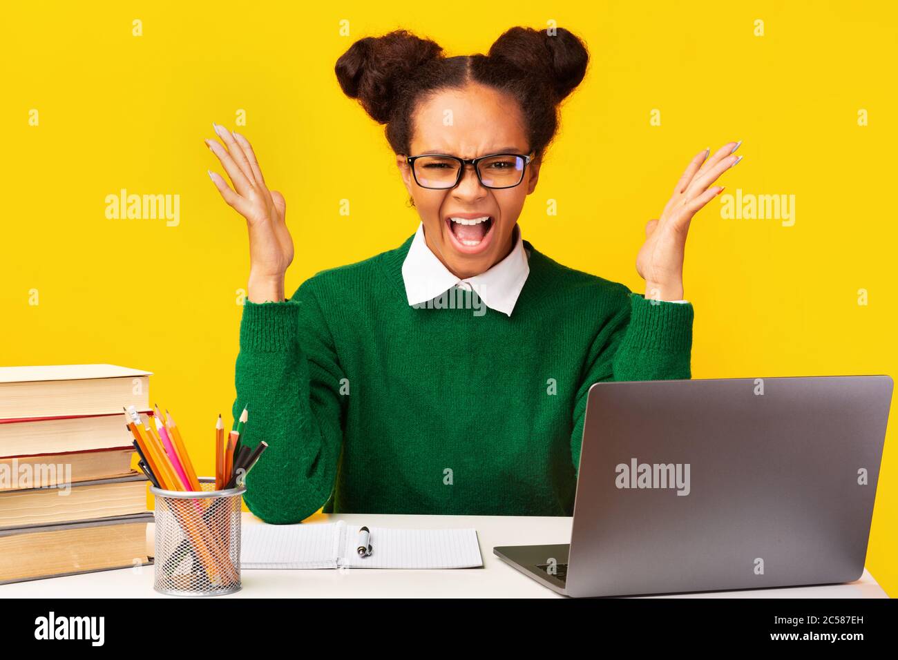 Nervous afro teen shouting sitting at desk Stock Photo