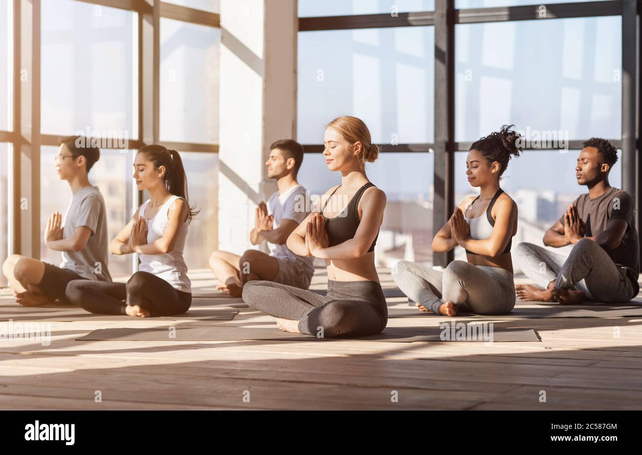 Meditation Session. Group Of Diverse Sporty People Practicing Yoga In Modern Gym Stock Photo
