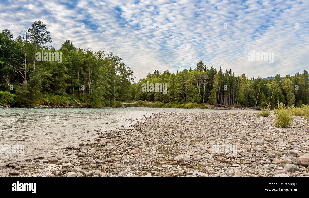 Sunset over the upper Kitimat River in Northern British Columbia, Canada, with a cloudy blue sky, confier woodland and gravel bar. Stock Photo