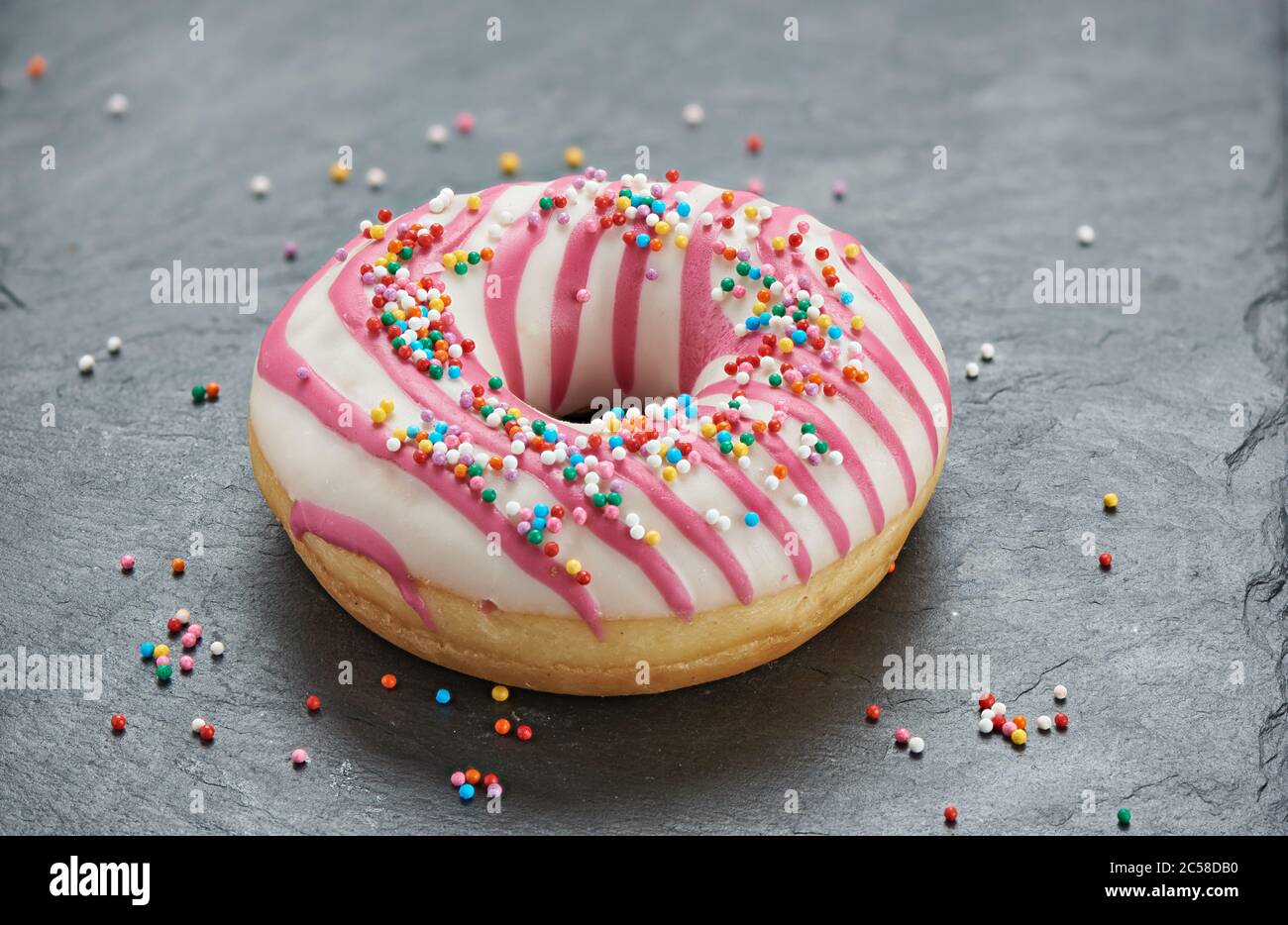 glazed round donut with sprinkles on a stone table Stock Photo