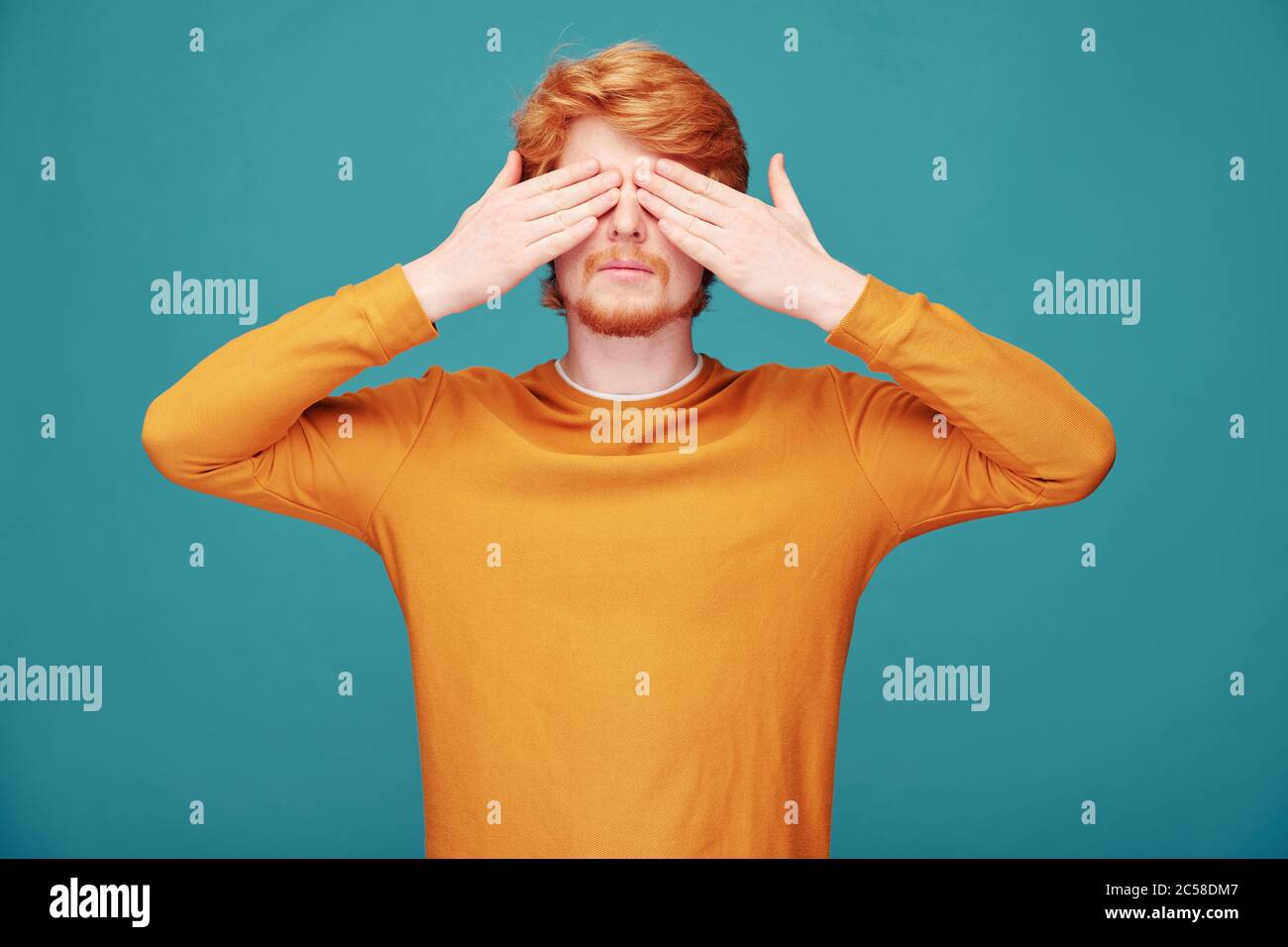 Calm young redhead man with beard closing eyes with hands in anticipation of surprise Stock Photo