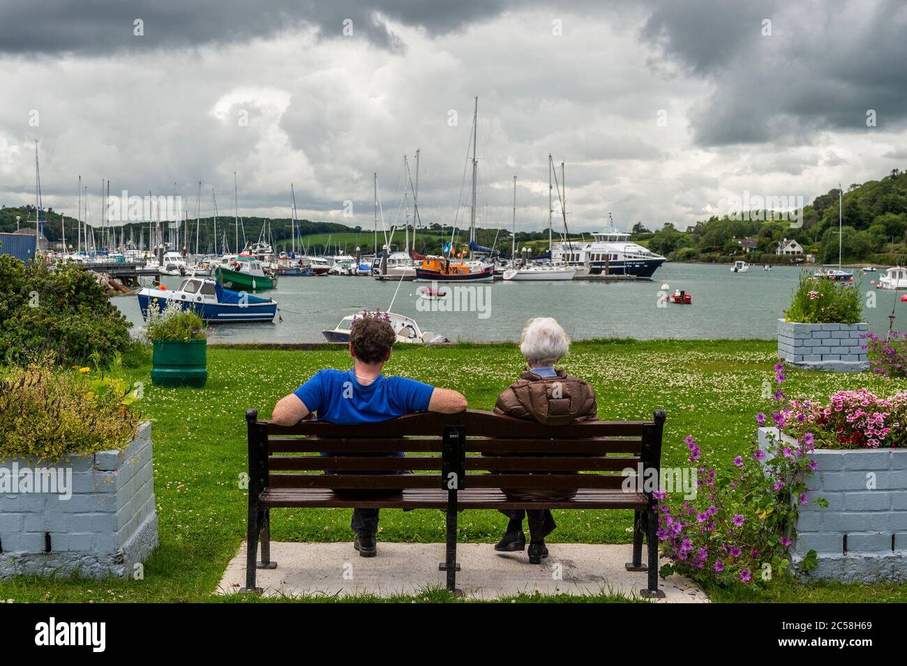 Crosshaven, West Cork, Ireland. 1st July, 2020. On a very warm, but overcast day, a couple sit on a bench overlooking Crosshaven Marina. Credit: AG News/Alamy Live News Stock Photo