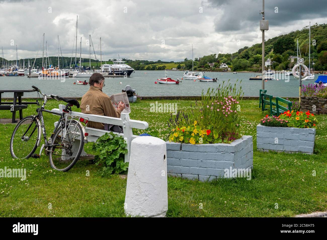 Crosshaven, West Cork, Ireland. 1st July, 2020. On a very warm, but overcast day, a man reads the paper on a bench overlooking Crosshaven Marina. Credit: AG News/Alamy Live News Stock Photo