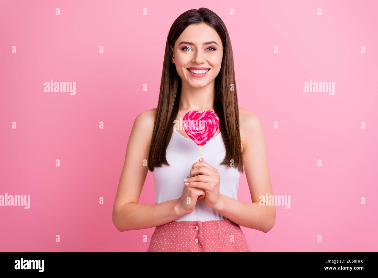Photo of charming funny lady hold big heart shape lollipop on stick want to try yummy dessert good mood wear white singlet dotted skirt isolated Stock Photo