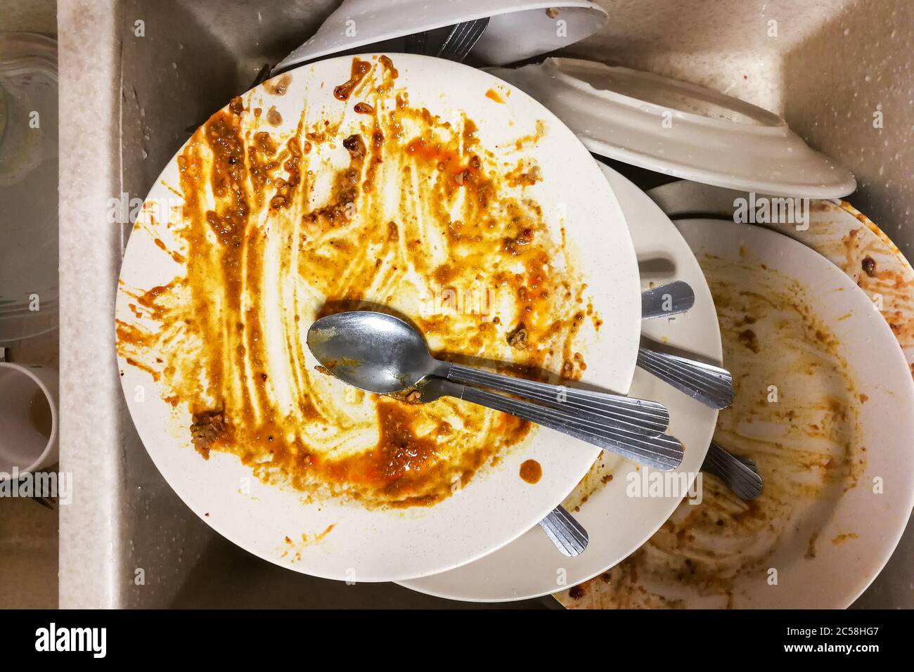 Dirty stack of unwashed oily dishes plates in wash basin at pantry