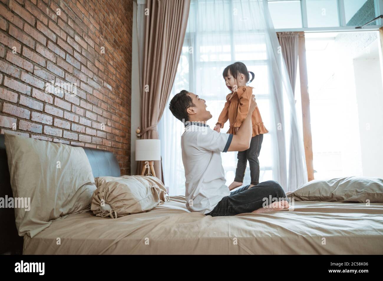 https://c8.alamy.com/comp/2C58K06/asian-father-plays-with-his-little-daughter-on-his-lap-while-sitting-on-the-bed-2C58K06.jpg