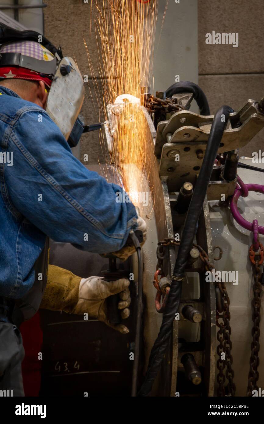 A welder grinding and welding on a metal pipe piece for industrial use