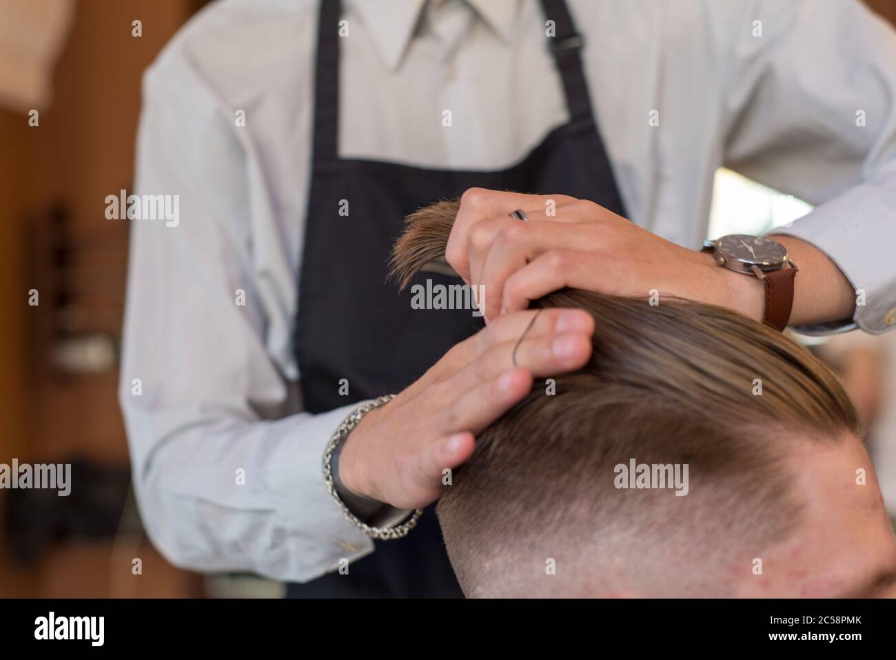 professional hands of hairdresser master styling hair for client barbershop, young guy. Hair care, collects hair in a ponytail, professional hair Stock Photo