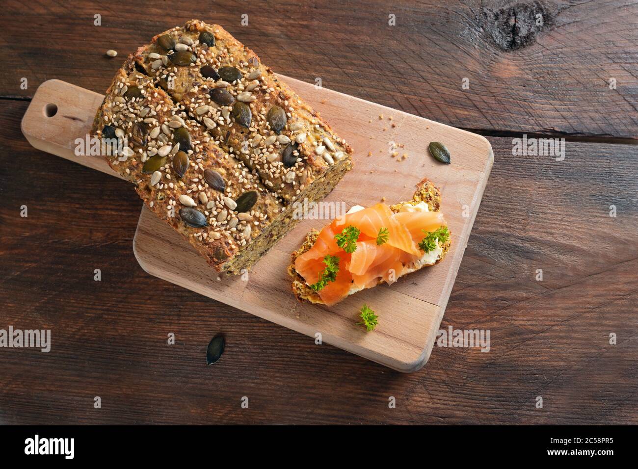 Healthy slimming with low carb or ketogenic diet, protein bread and sandwich with salmon and herb garnish on a cutting board and on a dark rustic wood Stock Photo